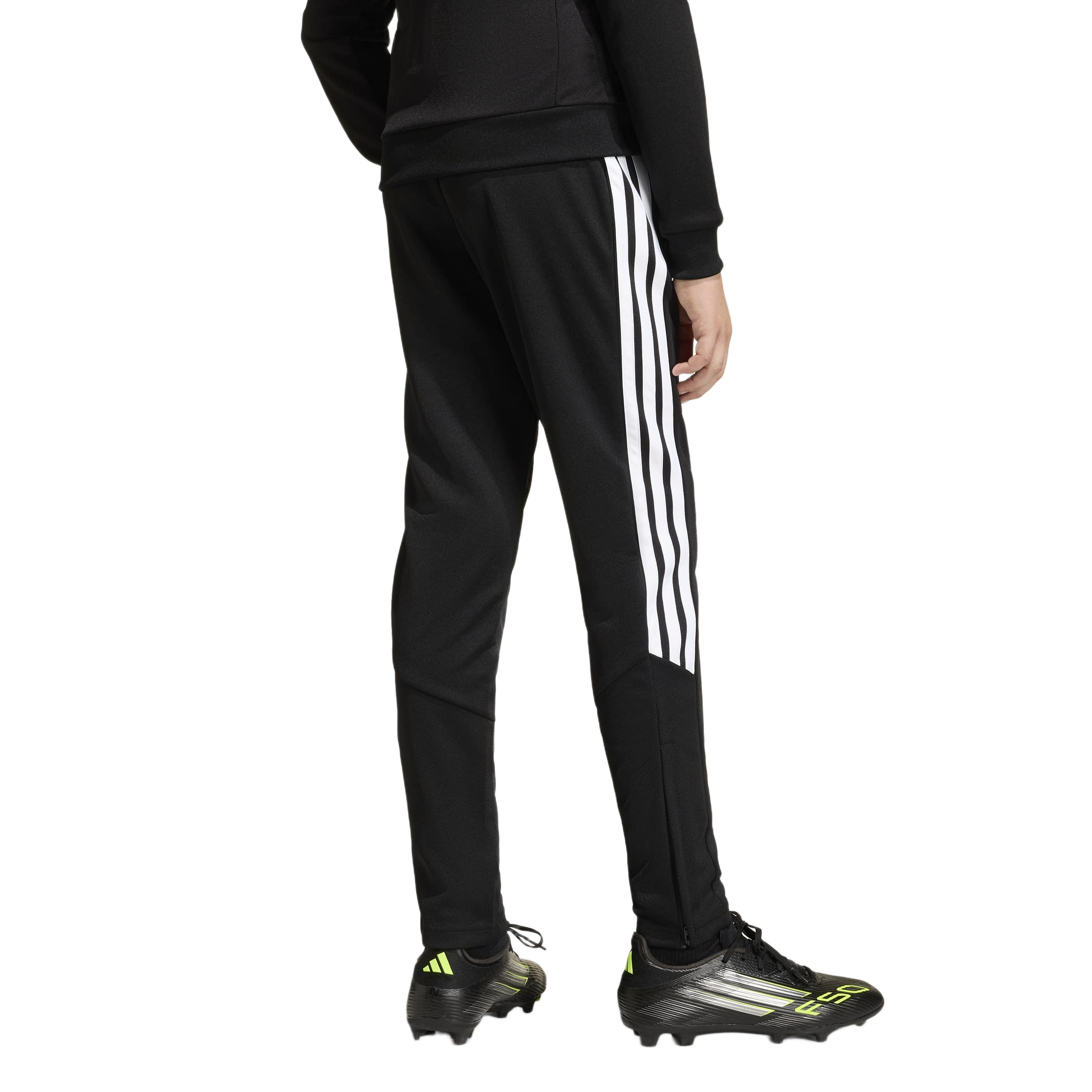 Rear view of a person in black Adidas track pants with white stripes and black F50 soccer cleats with neon accents on a white background.