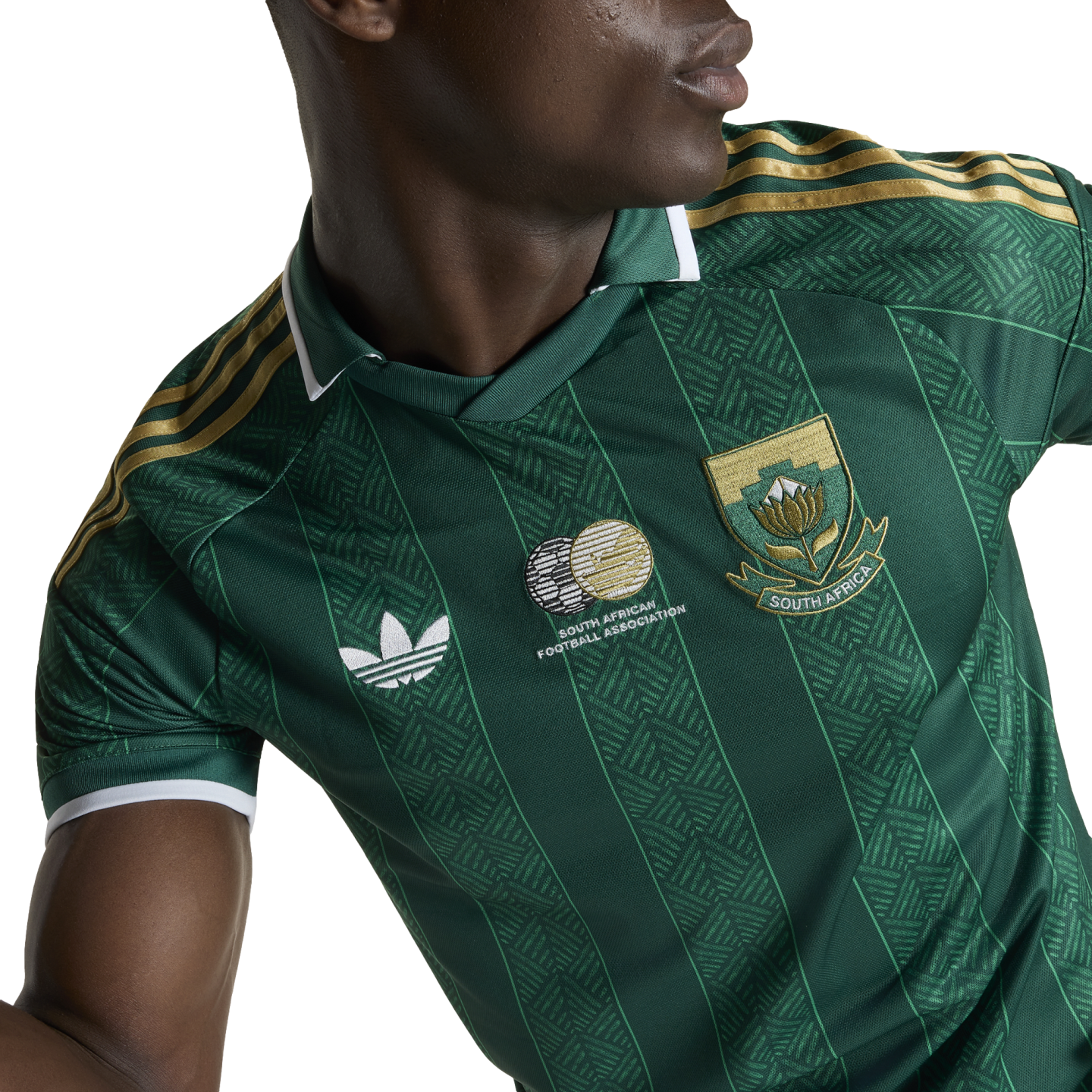 A person wearing a green South Africa national football jersey with gold shoulder stripes, a white Adidas logo, and the national team crest over a patterned fabric.