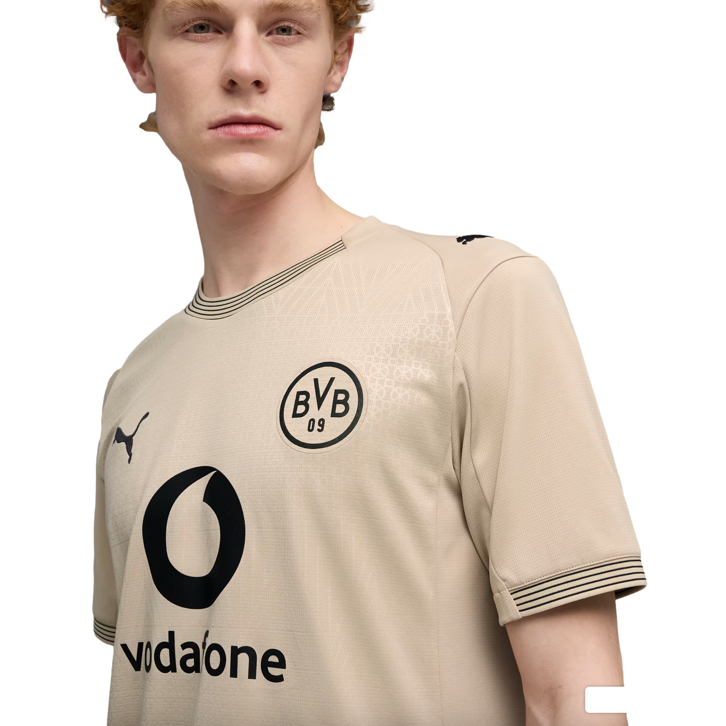 A young man with red hair wearing a tan BVB 09 soccer jersey by Puma with a black Vodafone logo, set against a plain black background.