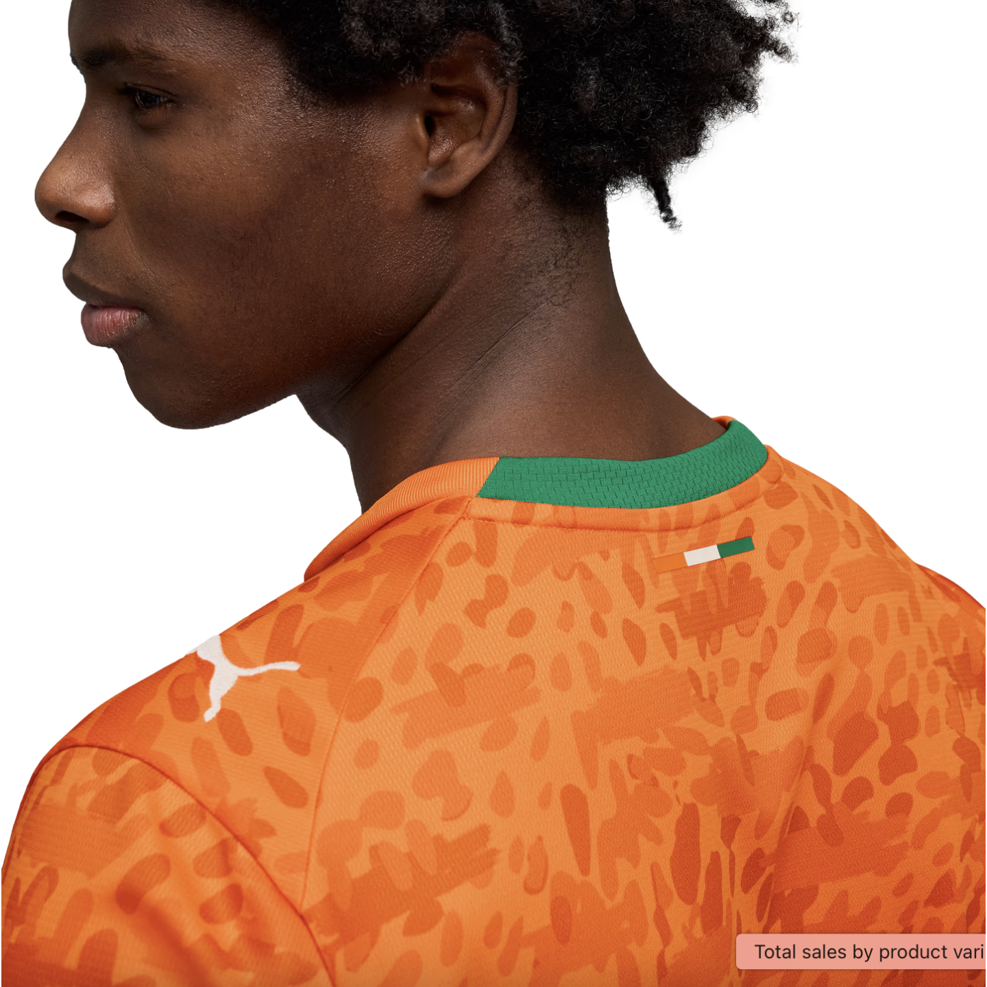 A profile view of a young man with dark curly hair wearing an orange Puma jersey against a black background. The jersey features a tonal abstract animal print, a white Puma logo on the shoulder, and a green collar with a small flag of the Ivory Coast on the back.