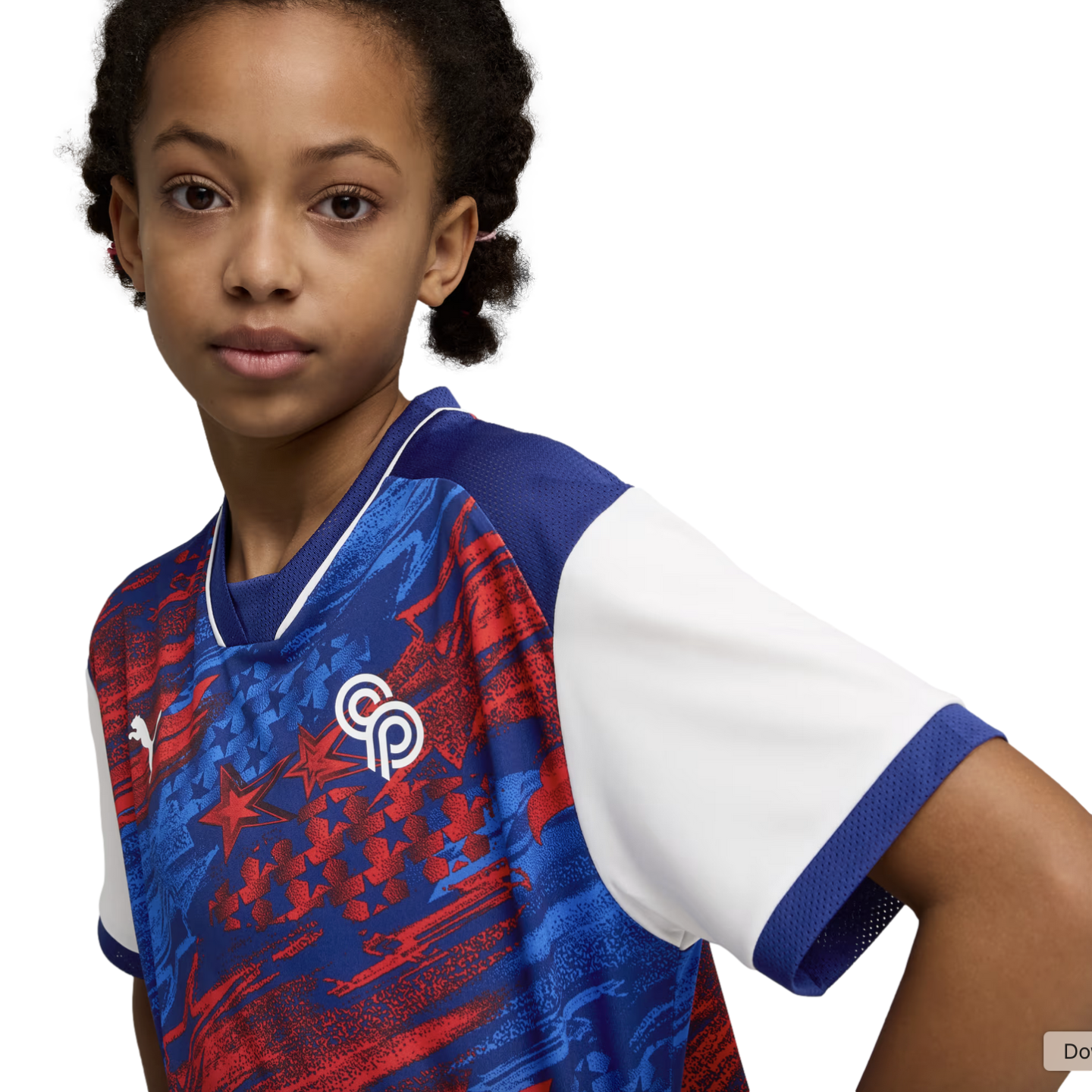 A young girl with brown skin and dark curly hair looks directly at the camera against a solid black background. She wears an athletic jersey with a blue, red, and white graphic pattern featuring stars, a white "CP" logo on the left chest, and a solid white right sleeve.