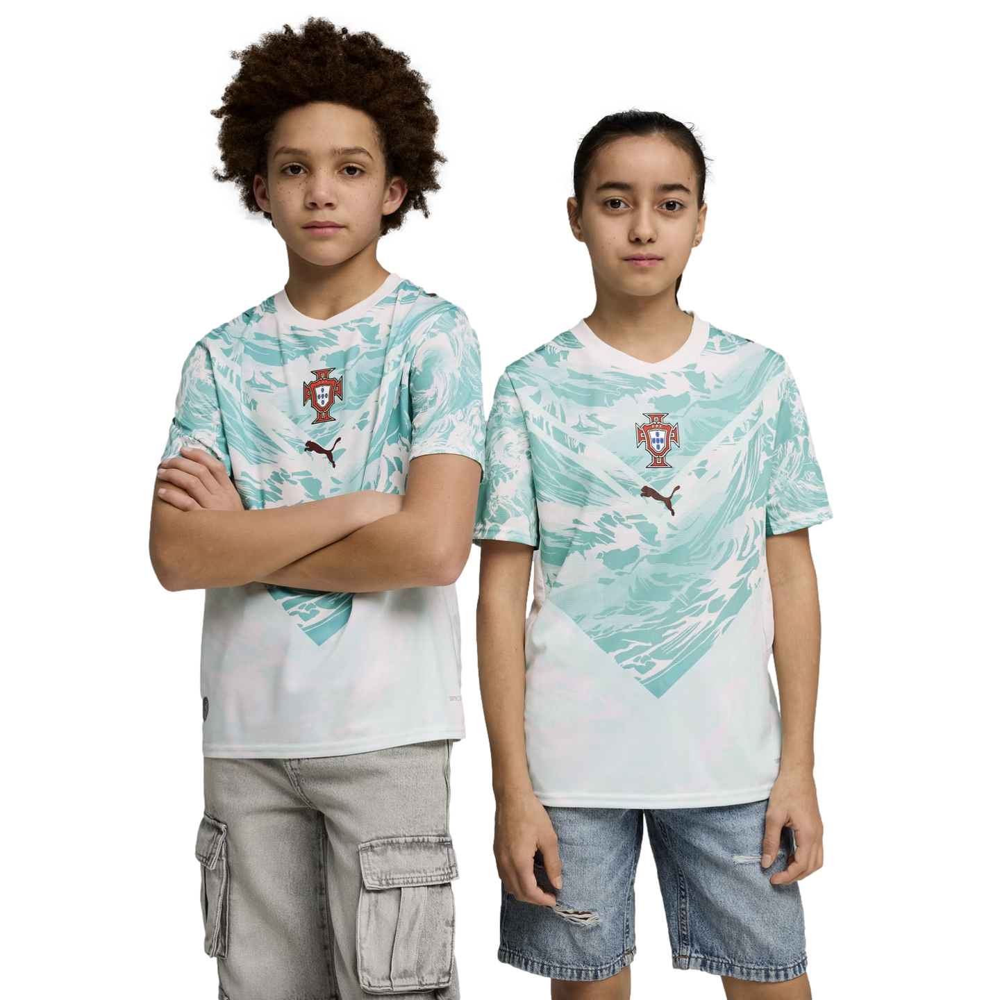 A boy and a girl stand side-by-side against a black background, wearing matching sports jerseys. The jerseys are white with a teal wave-like pattern on the upper half, featuring a team crest and a Puma logo in the center. The boy on the left has curly hair, crossed arms, and is wearing grey cargo shorts. The girl on the right is wearing denim shorts. Both children look directly at the camera with neutral expressions.