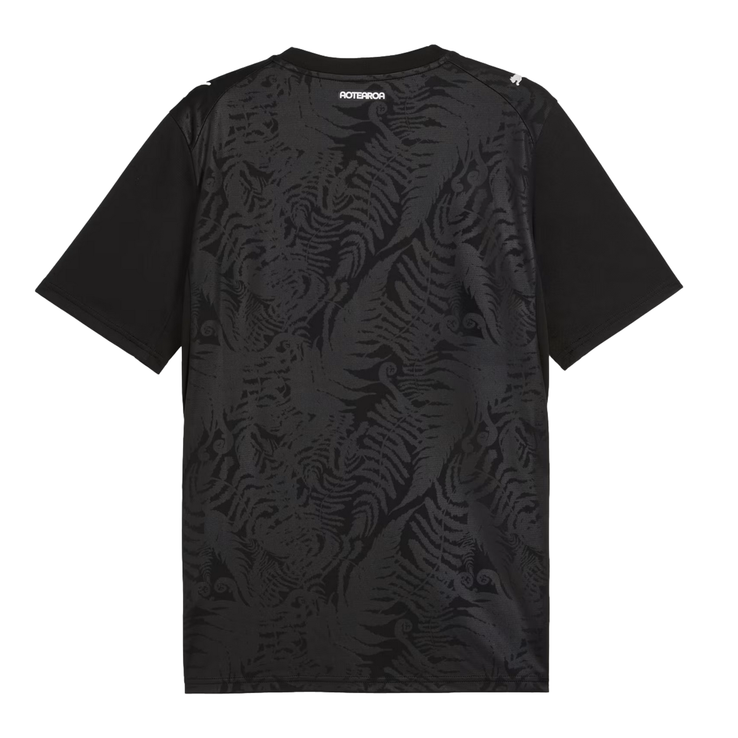 The back of a black t-shirt featuring a subtle, tonal pattern of repeating silver ferns. The word "AOTEAROA" is printed in white block letters below the collar, and a white Puma logo is on the right shoulder.
